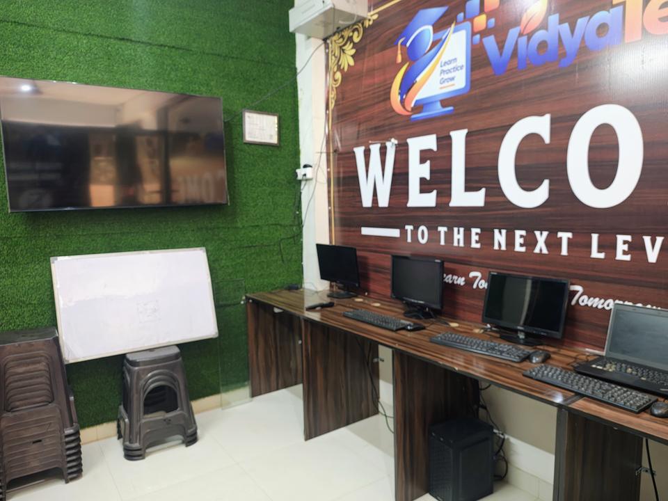 VidyaTech computer lab with desktop computers in front of the 'Welcome to the Next Level' wall and VidyaTech logo