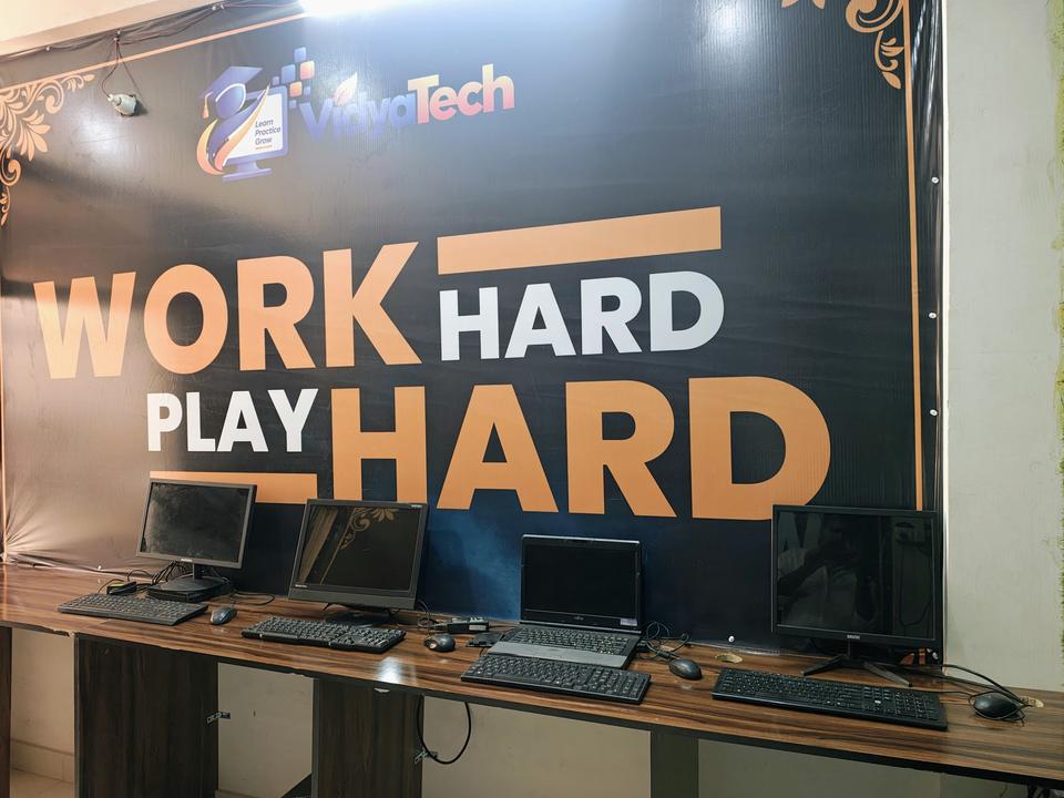 Row of computer workstations in front of the VidyaTech 'Work Hard, Play Hard' wall